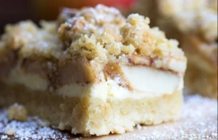 Apfel-Cheesecake mit Walnuss-Streuseln und Karamellsauce auf einem Teller.