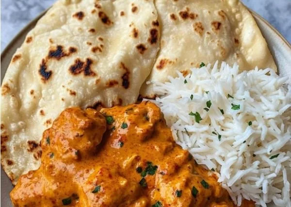 Butter Chicken Gericht auf einem Teller serviert mit Reis und frischen Kräutern.