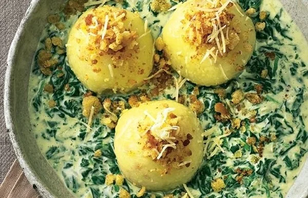 Kartoffelknödel mit cremiger Spinat-Käse-Soße auf einem Teller