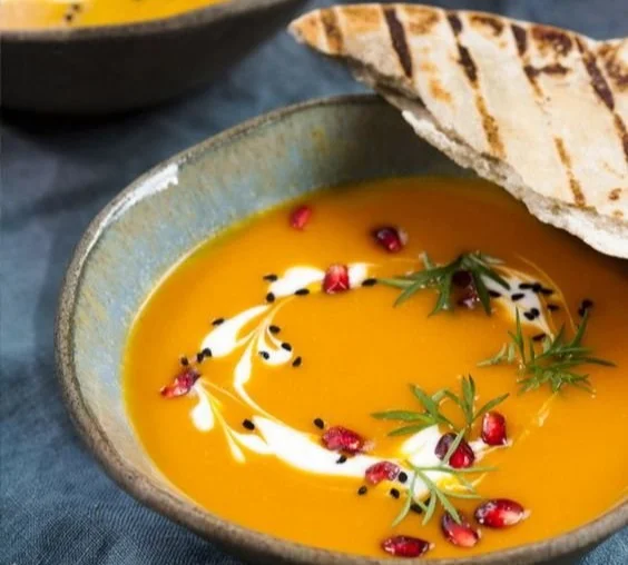 Kürbiscremesuppe in einer Schüssel mit frischen Kürbisstücken und Kräutern