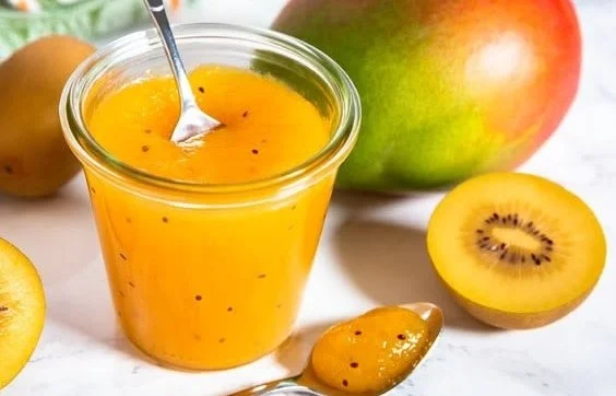 Hausgemachte Mango-Kiwi-Marmelade im Glas auf einem Holzbrett.